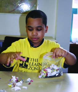 PHOTO BY CHUCK HOVEN Thursday, March 20, 2014, Fulton Branch, Cleveland Public Library, 3545 Fulton Road: Students from afterschool program of The Salvation Army’s Ohio City branch participate in a science program taught by staff of the OSU Extension Service. Charles Van Leer III, age 9, cuts up pieces of newspaper and paper towel to place in a plastic bag with some topsoil. The students are participating in an experiment to see how well various substances break down when composted.