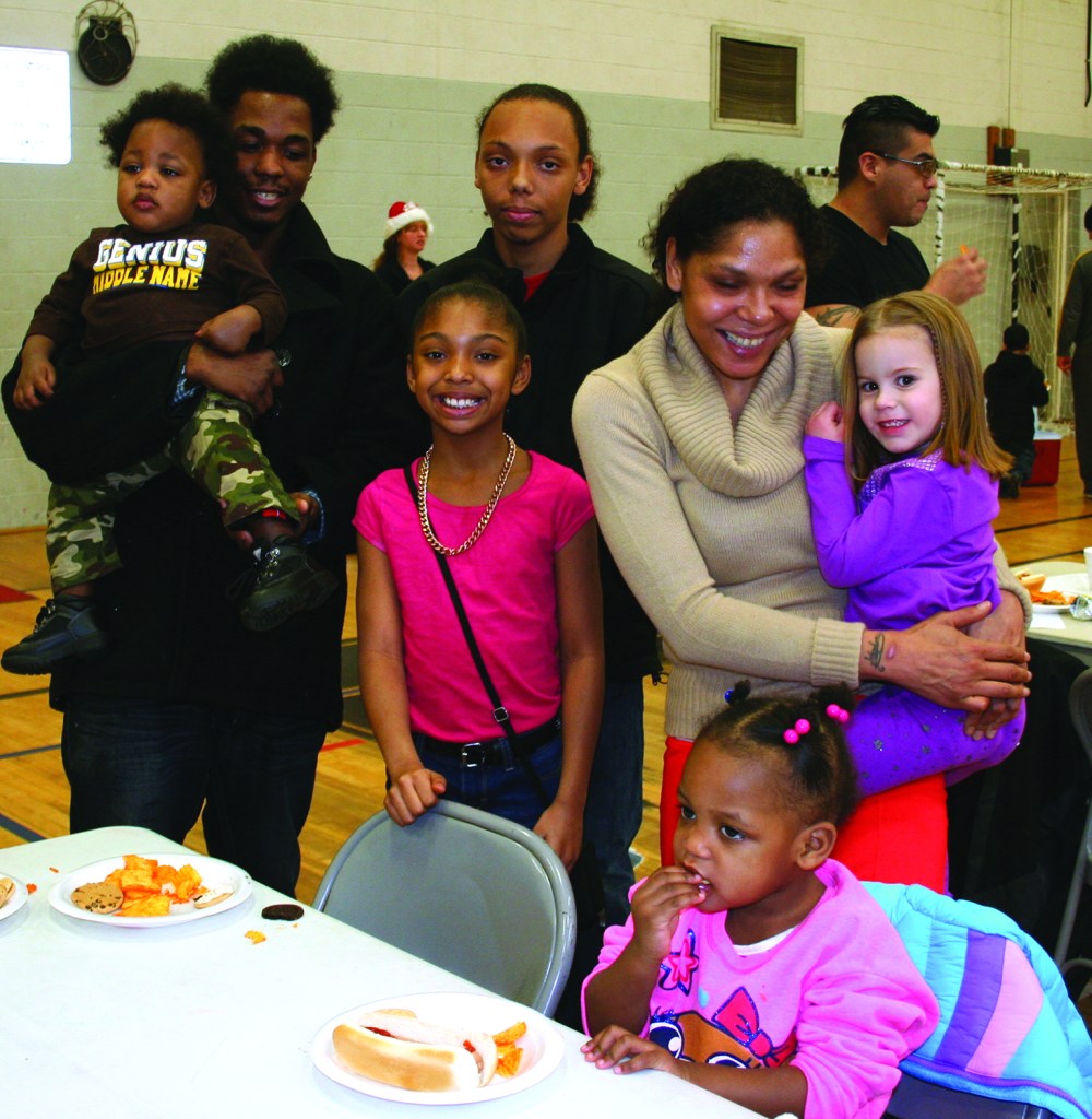 PHOTO BY DEBBIE SADLON Saturday, December 20, 2014; Zone Recreation Center Christmas Party, W. 65th and Lorain Avenue: (L-R) Top Row: SJ Burton, age 1, Stephen Burton, and Stephon Burton, Age 15. Second Row Makayla Burton, age 9, Christina Bruton and Kadence Burton age 4. Bottom seated at table: Sharonda Burton, age 2. Christina Burton and her family are enjoying some food at the Christmas Party while awaiting the arrival of Santa Claus. Demetrius Oliver of Oliver Paralegal and Credit Restoration Services joined with Zone Recreation Center Manager Monica Lelutiu to plan the party and secure gifts for an expected 200 children.