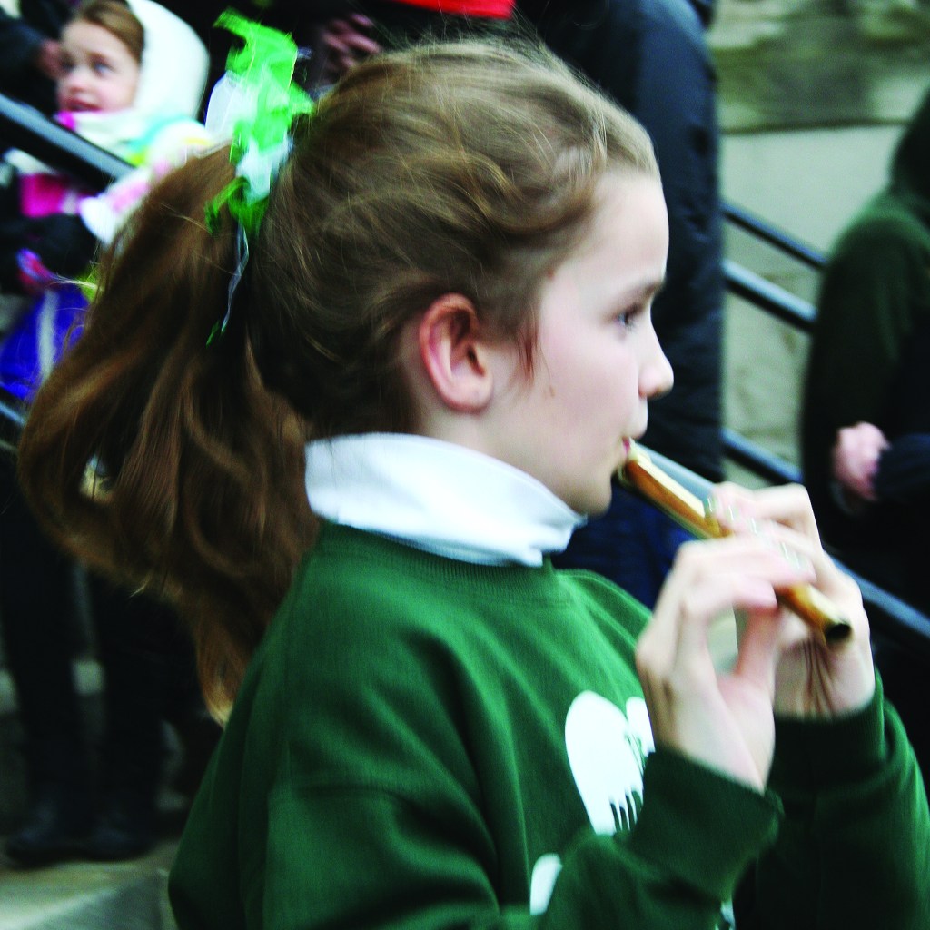 PHOTO BY DEBBIE SADLON Tuesday, March 17, 2015; St. Colman Church, 2027 W. 65th Street: A girl plays the tin whistle as she emerges from mass at St. Colman Church. West Side Irish American Club members traditionally attend mass at St. Colman Church prior to marching in the St. Patrick’s Day Parade in downtown Cleveland.