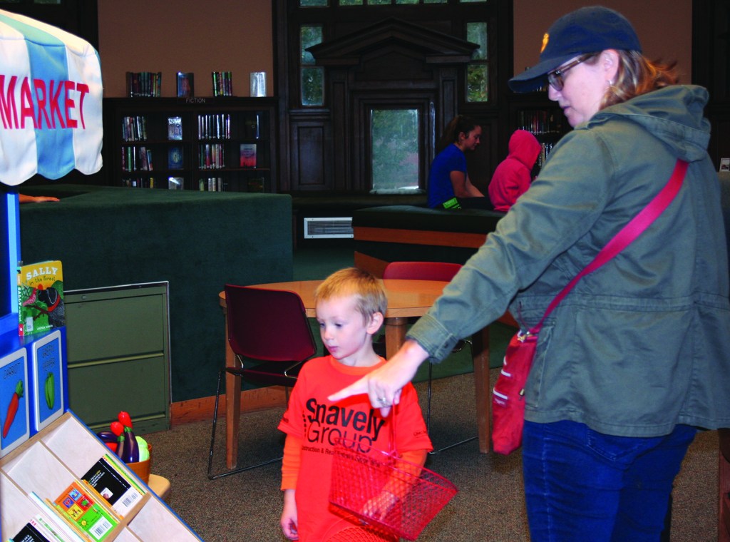 PHOTO BY DEBBIE SADLON Saturday, September 12, 2015; Carnegie West Library’s Family Learning & Literacy Play Space, 1900 Fulton Road: Brooke King points out some of vegetables in the farmers’ market truck to her son Oscar Fraunfelder, age 4. Oscar, spent the morning planting and harvesting the plastic vegetables in the Farmers’ Market Garden and retrieving eggs from the chicken coop. 