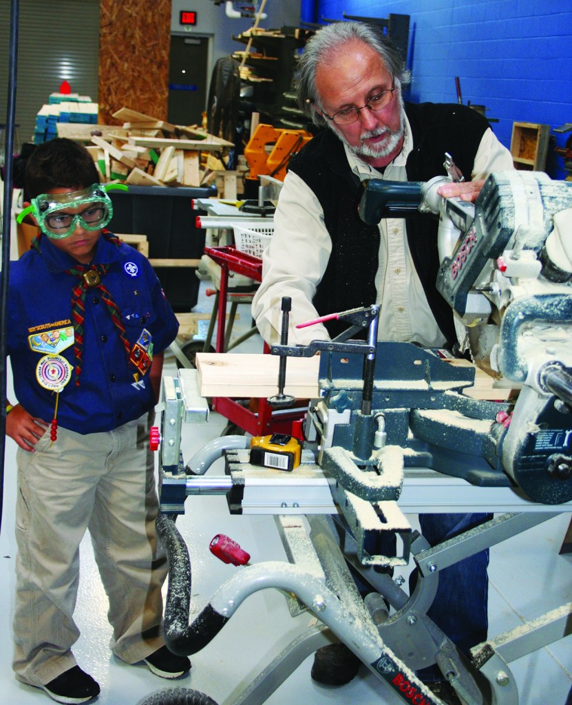 PHOTO BY CHUCK HOVEN Friday, October 16, 2015; Building Construction room, Max Hayes High School, 2211 W. 65th Street: Max Hayes Building Construction Instructors Jim MacDowell and Jim Mulgrew, Construction Curriculum Specialist John Nesta, and Max Hayes Building Construction students serve as hosts to guests from Olmsted Falls Cub Scout Pack 102. Max Hayes staff and students engaged their guests in building toolboxes. Here instructor Jim MacDowell shows Cub Scout Rafy Lofton, age 12, how to cut boards for the toolbox with a power saw while still keeping all ten fingers for future use. 