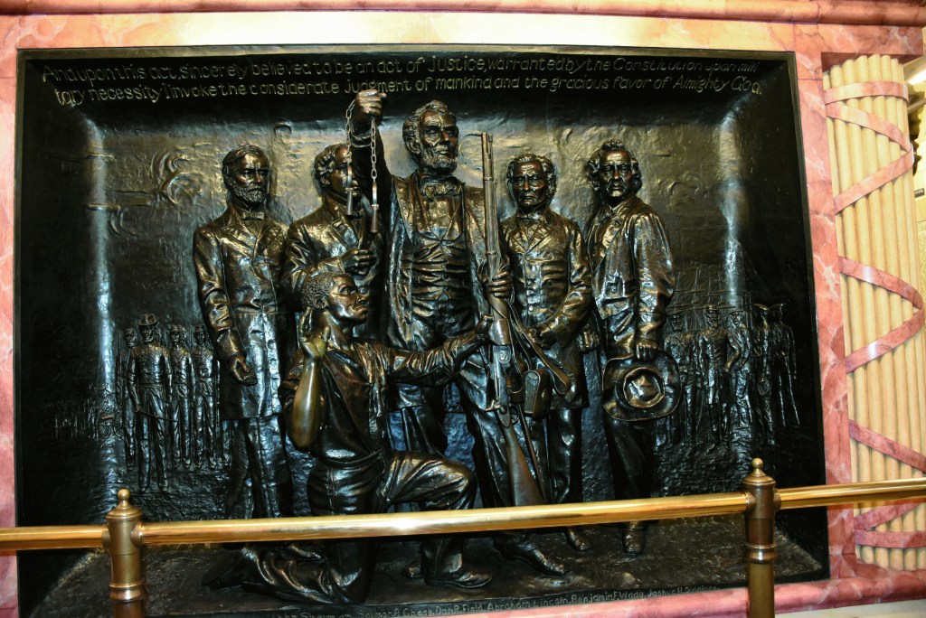 June 19, 2026; Soldiers and Sailors Monument, Cleveland Public Square: This panel inside the Soldiers and Sailors Monument is titled “The Emancipation of the Slaves.” The emancipation of the enslaved is represented by the open shackles in Abraham Lincoln’s right hand. The panel also depicts the establishment of the United States Colored Troops, represented by Lincoln handing a weapon to the newly emancipated man. The model for the man kneeling, Dan R. Fields, was born in the slave state of Louisiana. Fields fled to Ohio where he later participated in the construction of the Monument. Fields became a caretaker of the Monument once it was completed. The men standing behind Lincoln are major Ohio abolitionists – (L-R) John Sherman, Salmon P. Chase, Benjamin F. Wade, and Joshua R. Giddings.